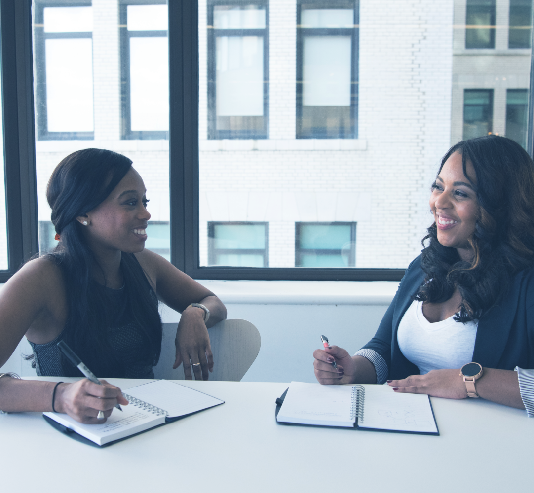 two women in a business setting smiling at each other as they work