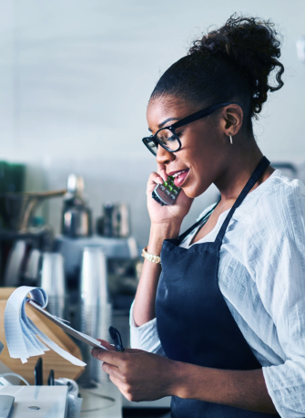 woman speaking on the phone while looking papers on a clip board